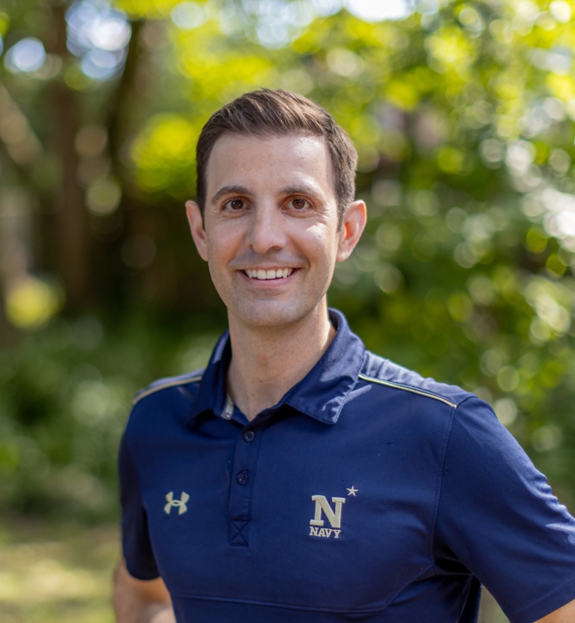 Photo of a man smiling in a dark blue polo with the U.S. Navy logo on the chest.