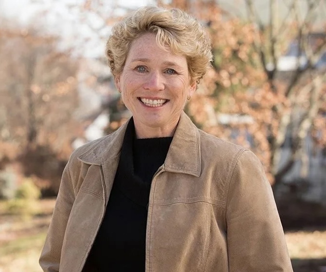 Photo of a woman smiling in a black shirt and tan jacket