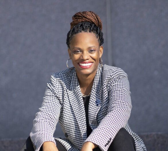 Photo of woman sitting on stairs smiling in black pants and a grey blazer.