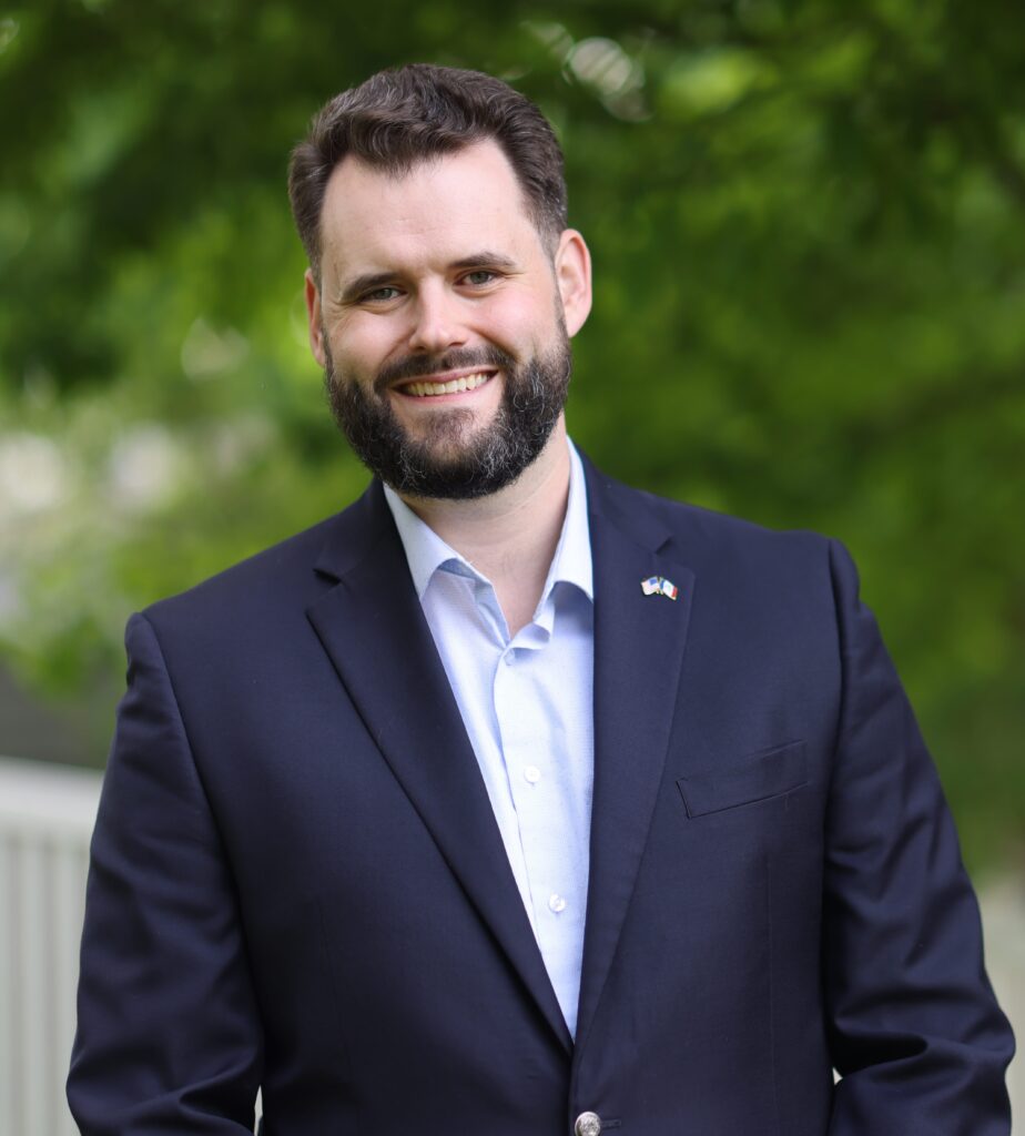 photo of a man smiling in a light blue button down and dark blue blazer.